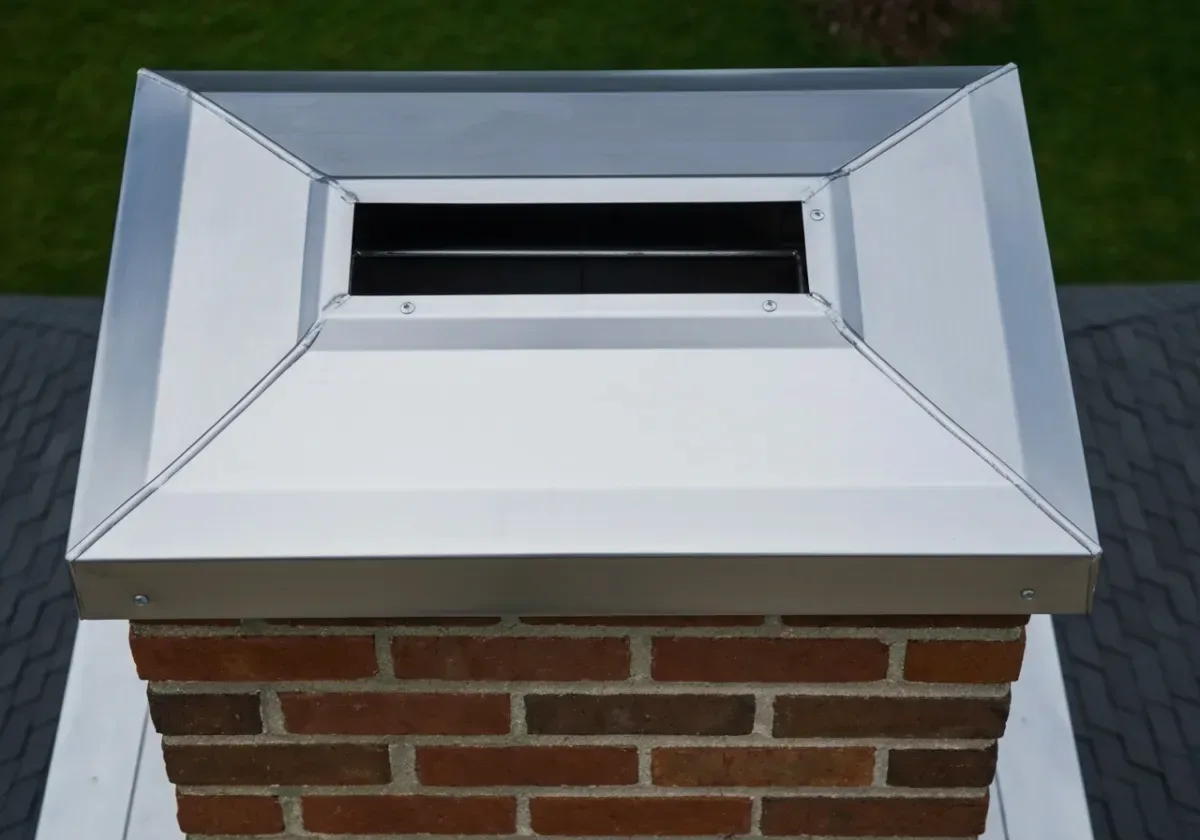 After — chimney cap installation: A bare, wide-open flue topped with a stainless cap against rain, salt air and nesting animals.